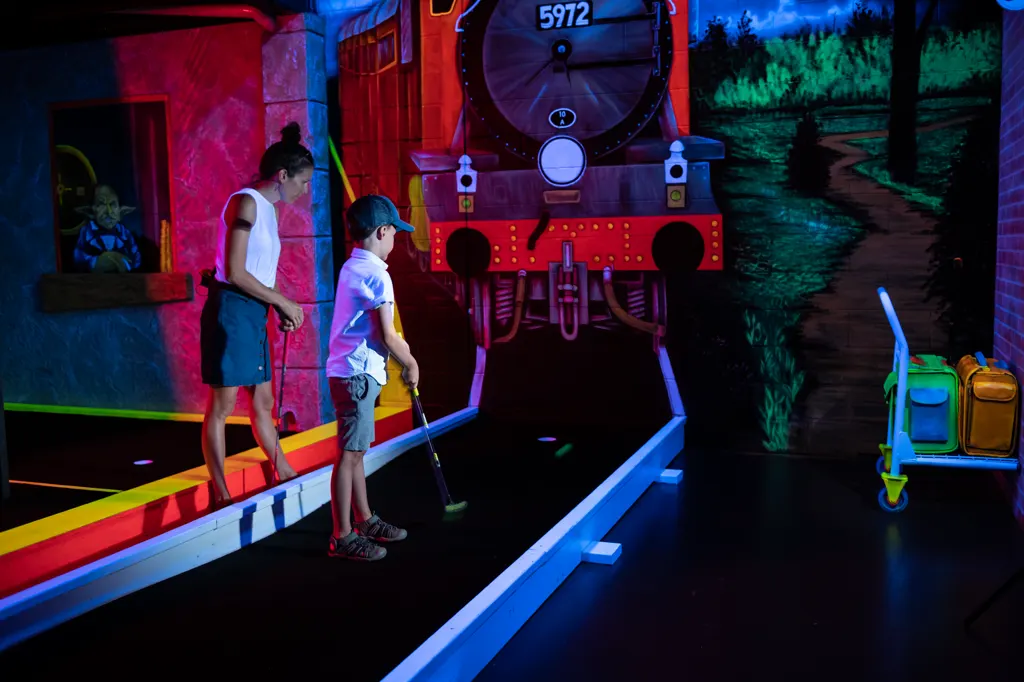 Parent et enfant qui jouent au mini-golf fluo intérieur à Drummondville pendant l'hiver